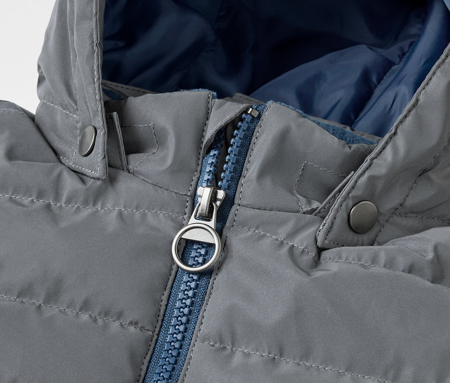 Detailansicht einer grauen, gesteppten Reflektierende Kinder-Steppjacke mit blauem Reißverschluss.