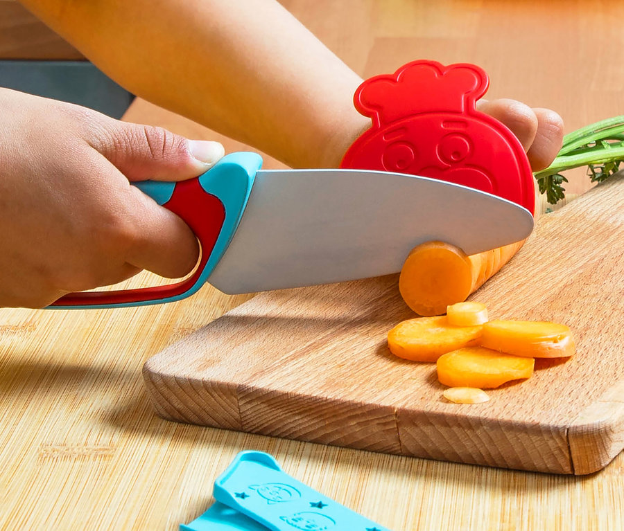 Kind schneidet Karotte mit Messer aus dem Chefclub Koch-Set auf Holzbrett.
