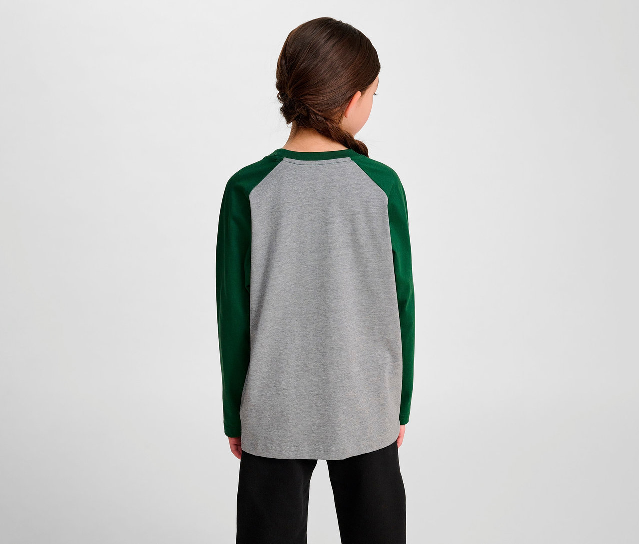Mädchen von hinten trägt ein grünes HUMMEL HMLJR Raglan Loose T-Shirt BEE mit langen Ärmeln und eine schwarze Hose.