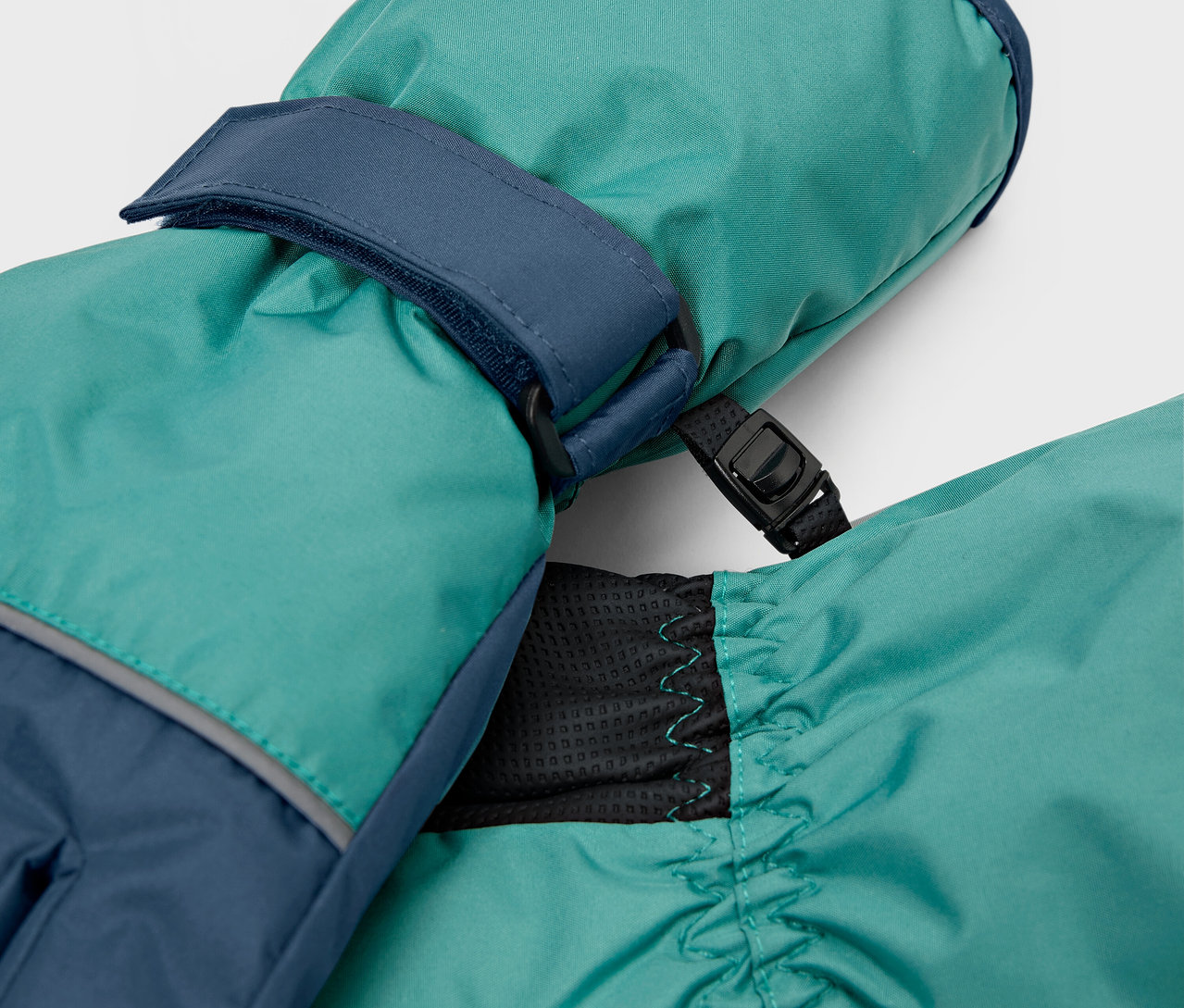 Nahaufnahme von türkisfarbenen Fäustlingen mit marineblauen Details.