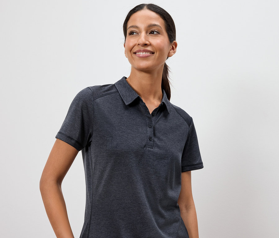 Frau trägt ein dunkelgraues Poloshirt vor einem weißen Hintergrund.