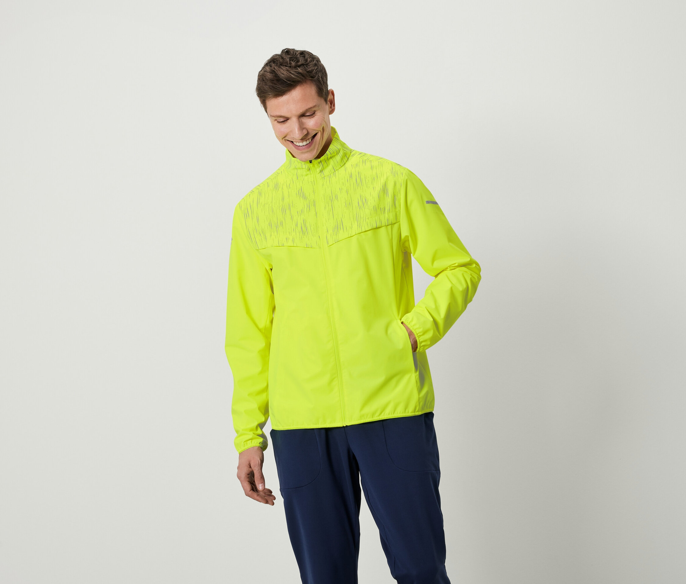 Ein lächelnder Mann posiert in einer neongelben Jacke und dunkelblauen Hosen.