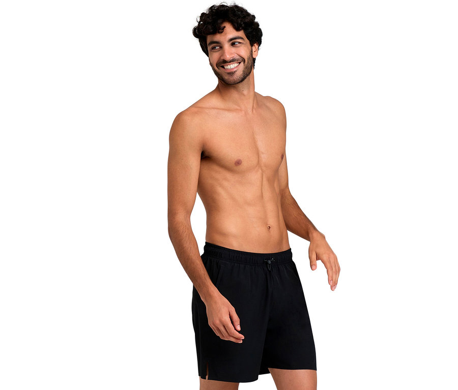 Lächelnder Mann mit lockigem Haar, der schwarze arena Evo Badeshorts trägt.