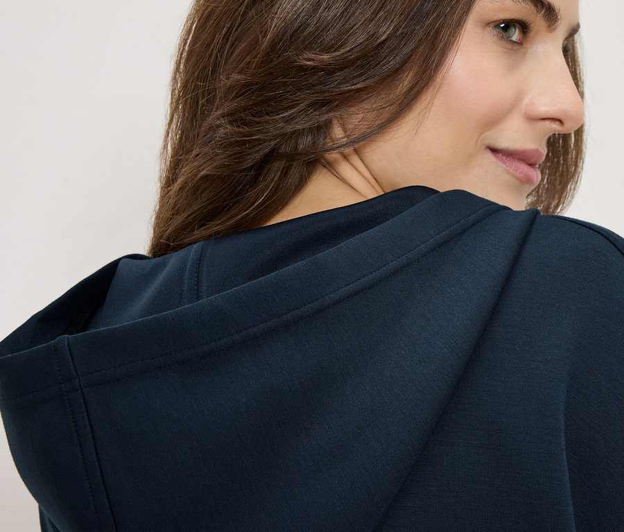 Frau trägt einen marineblauen Hoodie, Blick über die Schulter.
