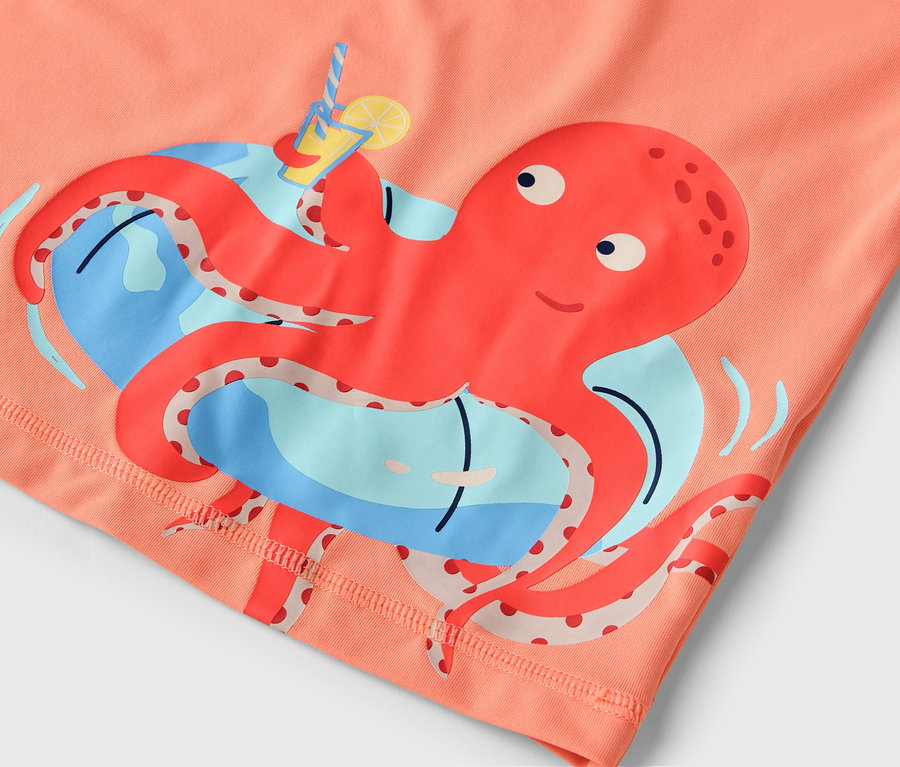 Nahaufnahme eines orangefarbenen Stoffes mit einem aufgedruckten roten Oktopus, der ein Getränk hält, vor einem blauen Hintergrund.