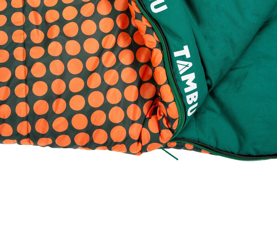 Ein grüner Schlafsack mit orangefarbenen Punkten liegt teilweise geöffnet und zeigt das grüne Innenfutter und das weiße Markenlogo.