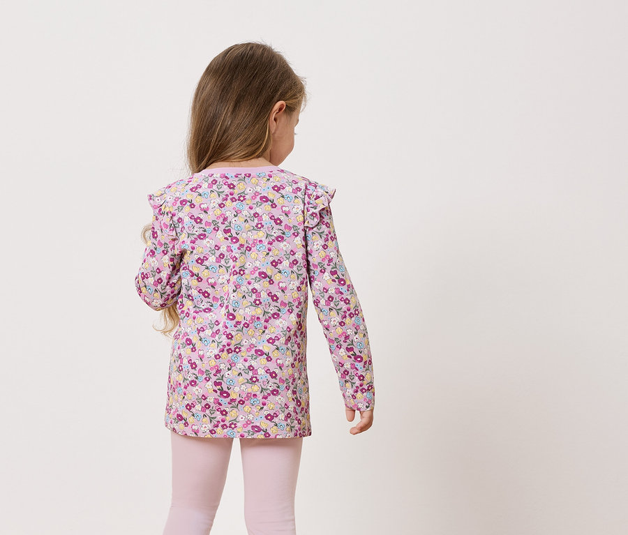 Rückansicht eines kleinen Mädchens mit langen Haaren, das ein langärmliges, blumengemustertes Oberteil und rosafarbene Leggings trägt.