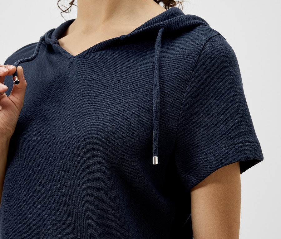 Nahaufnahme einer Frau, die einen marineblauen Kapuzenpullover mit kurzen Ärmeln trägt und eine Kordel hält.
