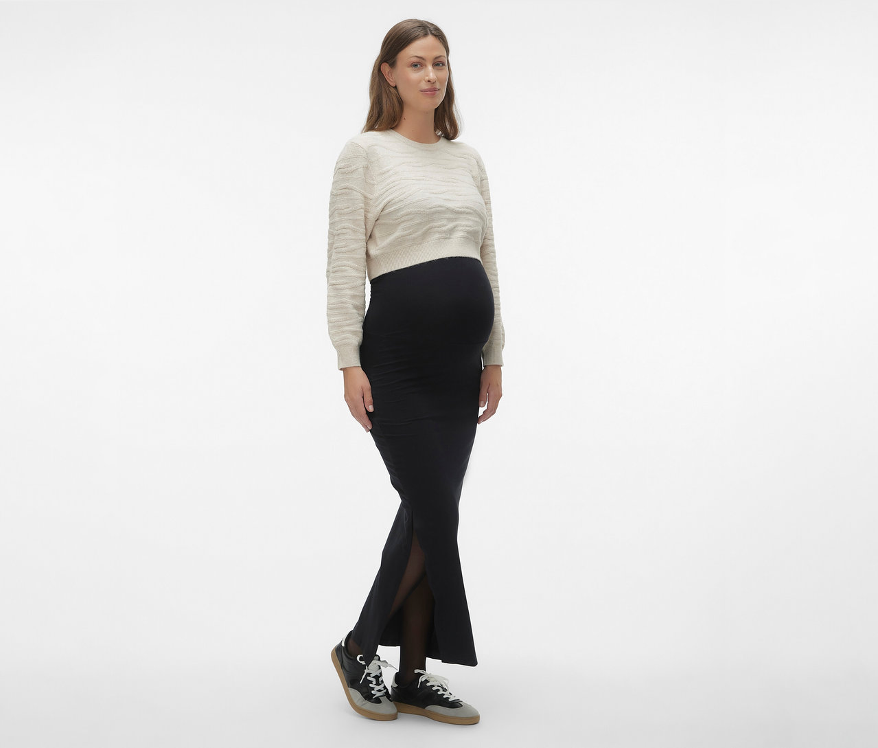 Frau trägt MAMALICIOUS Maxirock »MLEMMA TUBE« in Schwarz, dazu einen hellen Pullover und Turnschuhe.