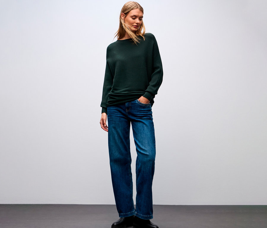 Eine Frau trägt einen Street One Strukturpullover, Jeans und Schuhe.