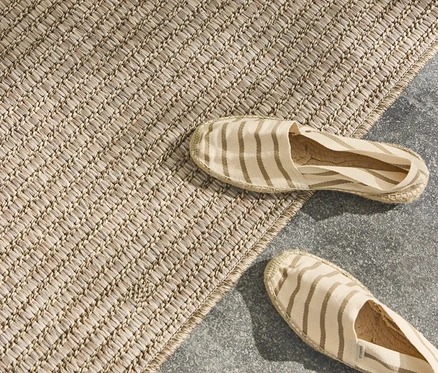 Gestreifte Espadrilles liegen auf einem beige Teppich auf einem grauen Untergrund.