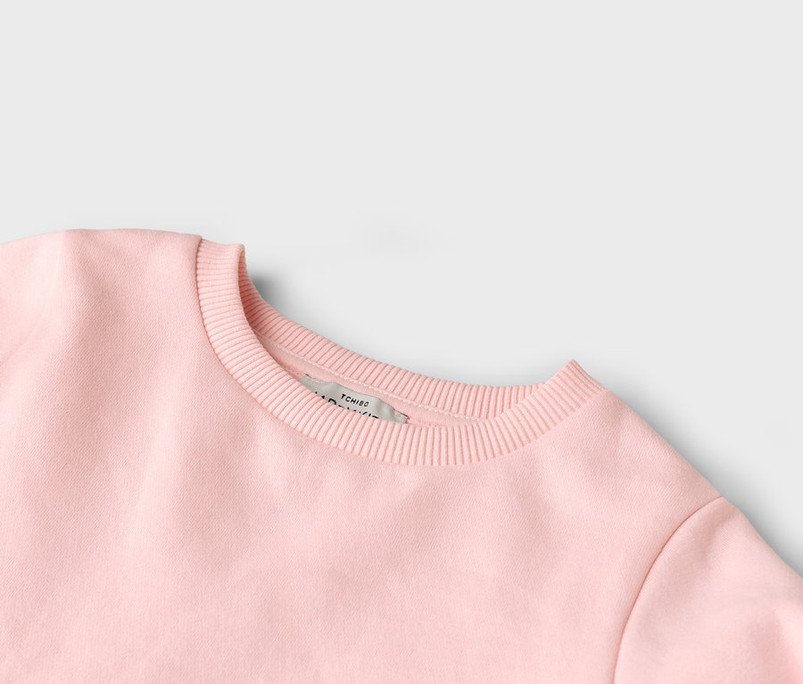 Nahaufnahme von einem rosa Pullover mit Rundhalsausschnitt und einem Tchibo-Etikett.