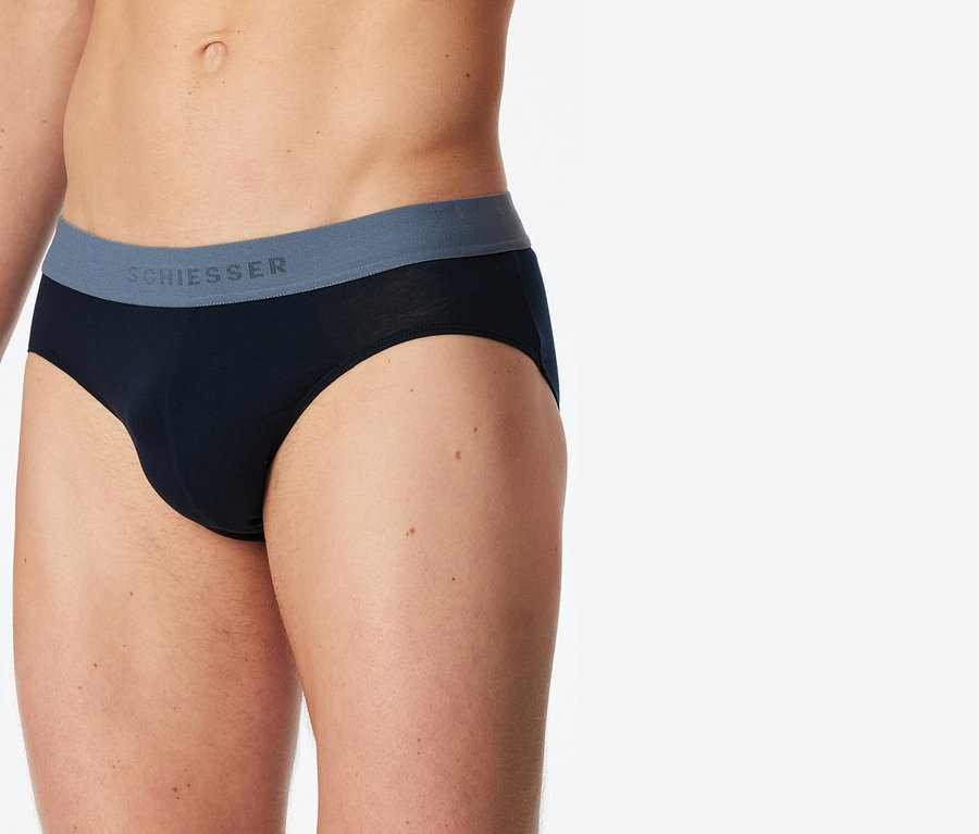 Nahaufnahme einer Person, die schwarze Schiesser-Slips mit grauem Bund trägt.