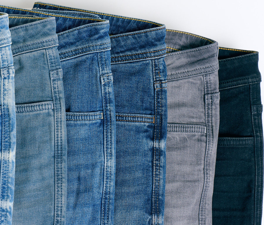 Fünf Jeans in verschiedenen Blautönen, Grau und Schwarz liegen übereinander.