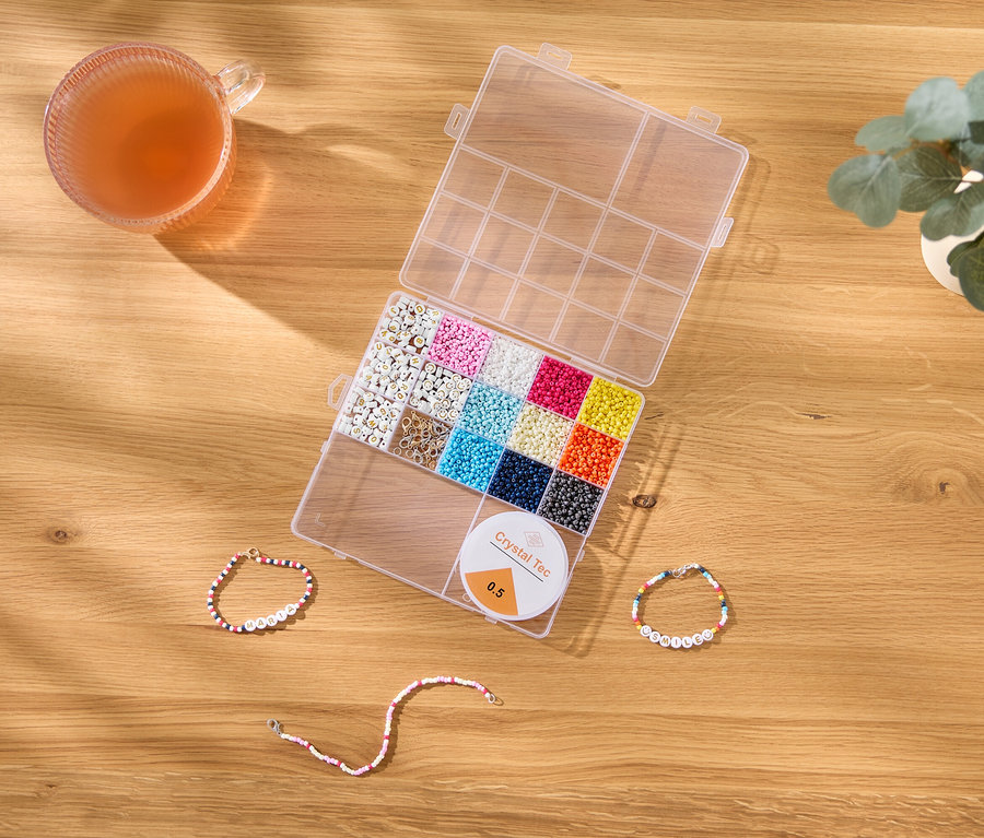Auf einem Holztisch liegen eine Tasse, eine Perlenbox, eine Spule Crystal Tec und drei Perlenarmbänder.