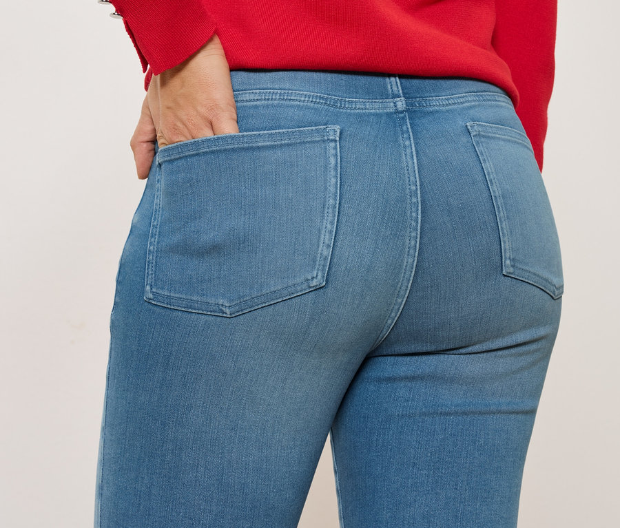 Nahaufnahme einer Person in blauen Jeans mit einer Hand in der Gesäßtasche, getragen mit einem roten Oberteil.
