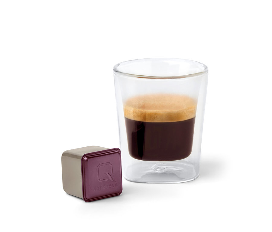 Eine Qbo Espresso ORO TOLIMA Kapsel neben einer Tasse Espresso.