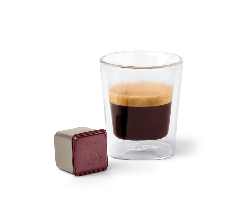 Eine Qbo Caffè KINYAA GALERAS Kapsel steht neben einem Glas Kaffee.
