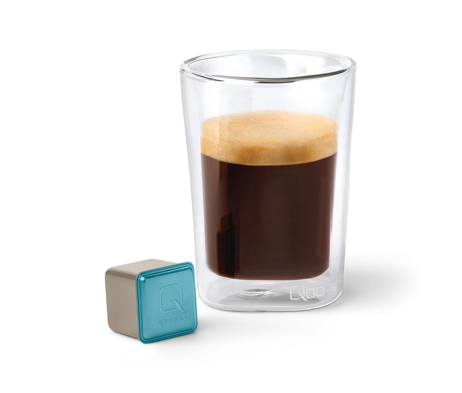 Qbo Caffè Grande KIRINYAGA BAYA Kapsel neben einem Glas Kaffee.
