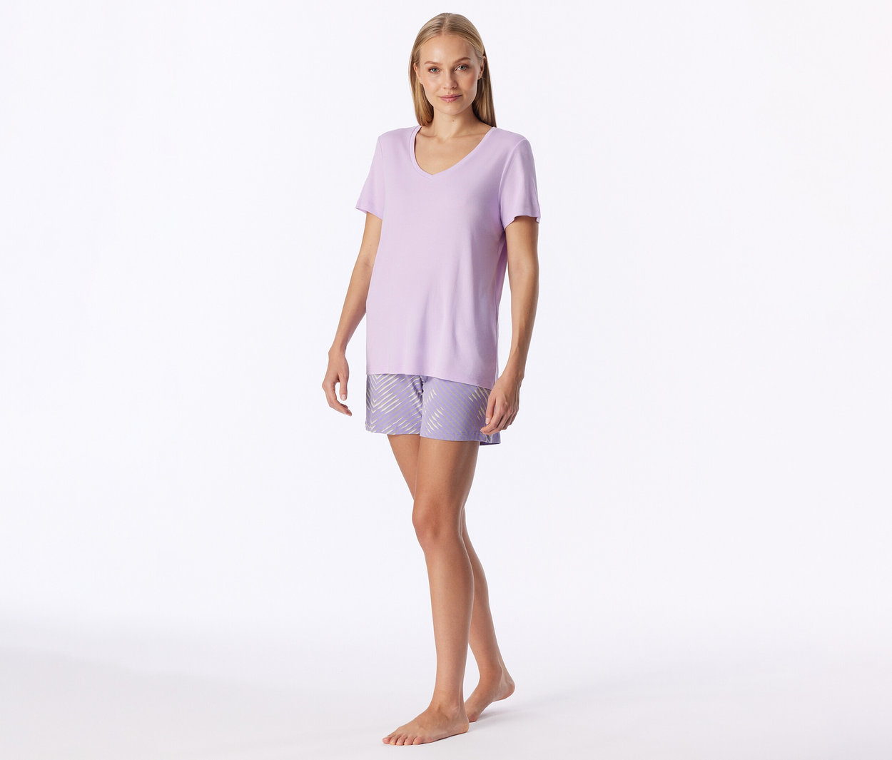 Frau steht in hellviolettem V-Ausschnitt-T-Shirt und gemusterten Shorts mit diagonalen Streifen, barfuß.