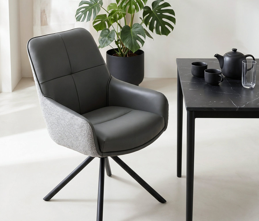 Ein modernes Zimmer mit einem dunkelgrauen Stuhl, einem schwarzen Tisch mit Marmorplatte, einer Teekanne und Tassen sowie einer großen Monstera-Pflanze in einem schwarzen Topf.