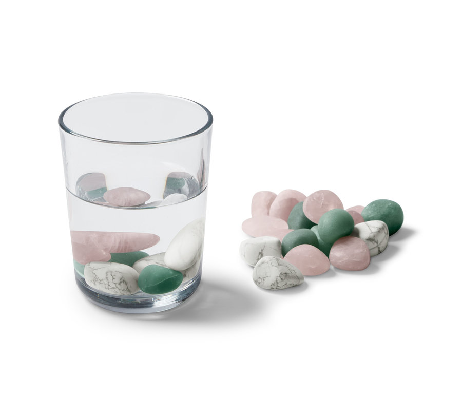 Ein Glas Wasser mit Wasser-Steinen darin und ein Haufen Wasser-Steine daneben.