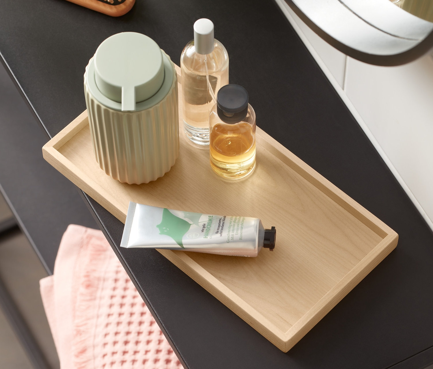 Schminktisch mit Tablett aus Holz, Seifenspender, Flaschen und Handtuch.