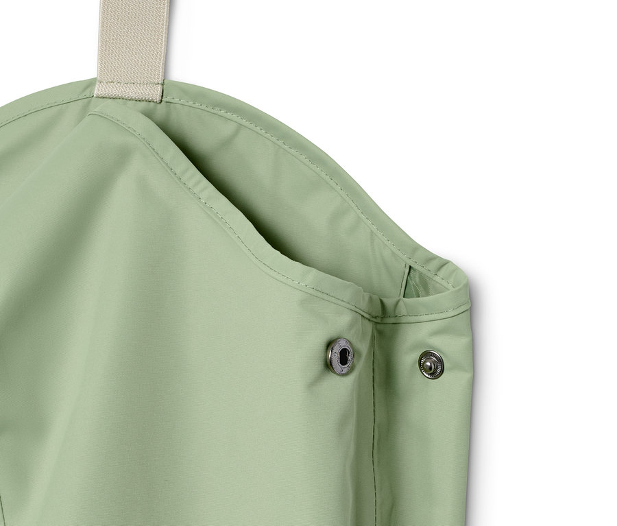 Detailaufnahme einer grünen Regenhose mit Latz und Druckknöpfen.