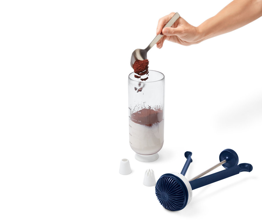 Eine Hand gibt mit einem Löffel Pulver in den Messbecher des 2-in-1-Dessert-Blitz.