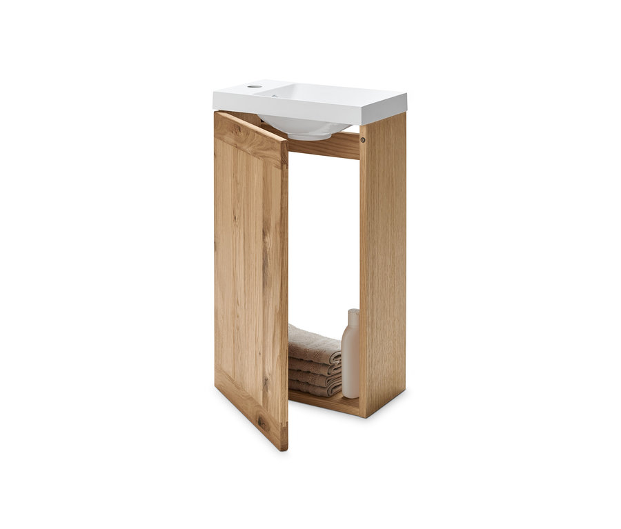 Gästewaschbecken mit Unterschrank, die Tür ist geöffnet, darin liegen gefaltete Handtücher und eine Flasche.