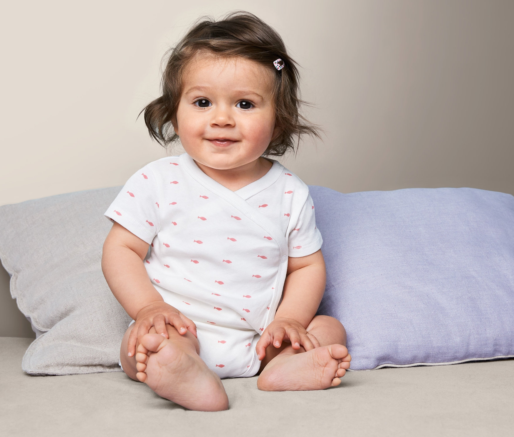 Ein Baby sitzt auf Kissen und trägt einen Baumwollbody.