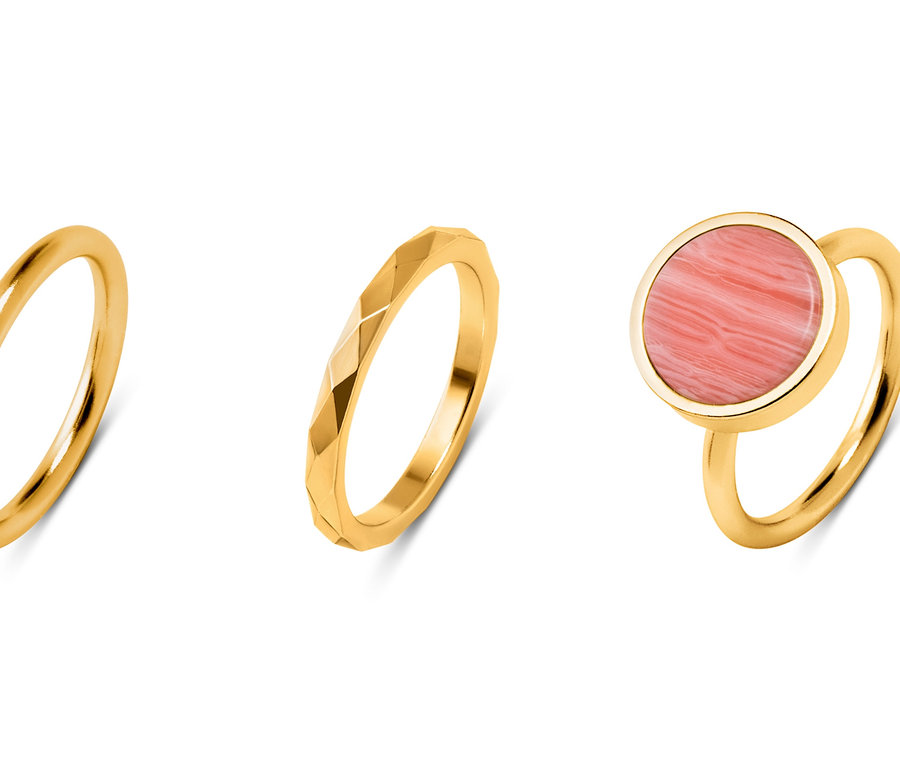 Drei goldene Ringe. Einer glatt, einer mit Dekor und einer mit einem rosa Stein.