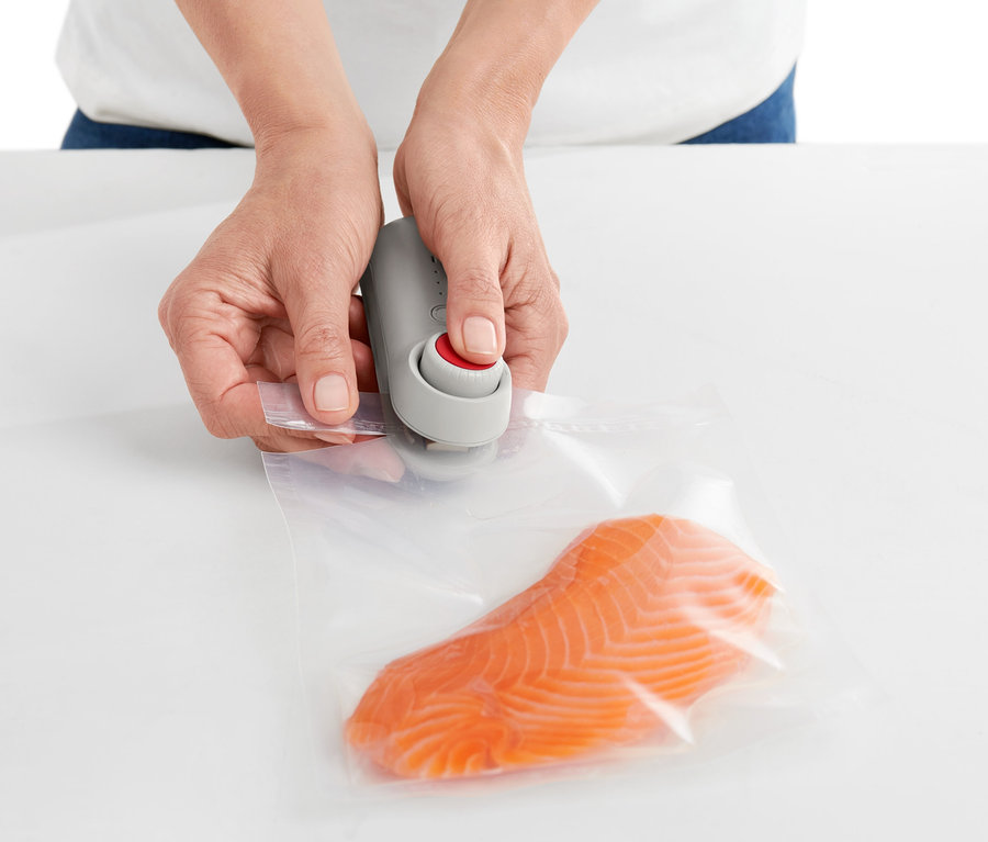 Frau benutzt ein Mini-Folienschweißgerät, um eine Tüte mit Lachs zu verschließen.