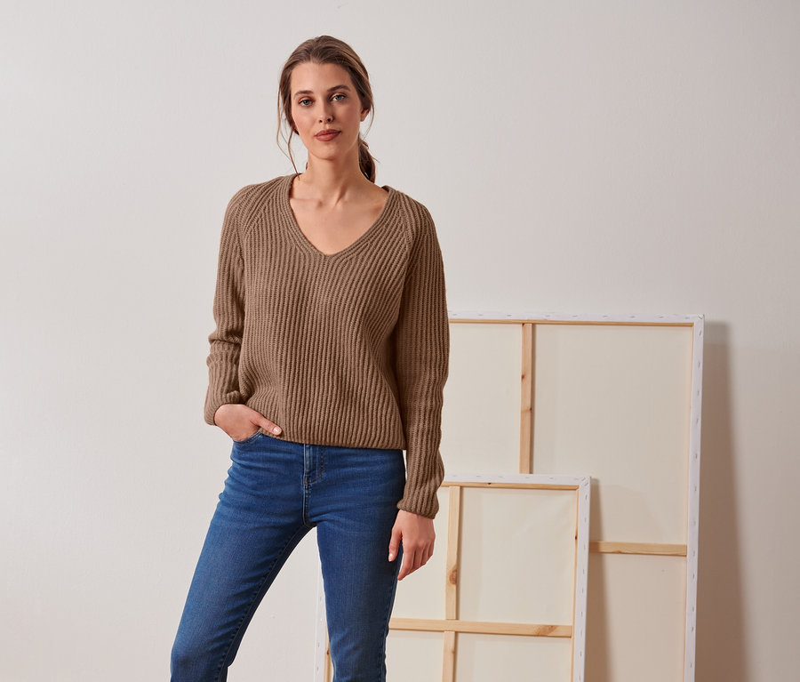 Frau posiert in beigem Grobstrick-Pullover mit Wolle und Jeans.