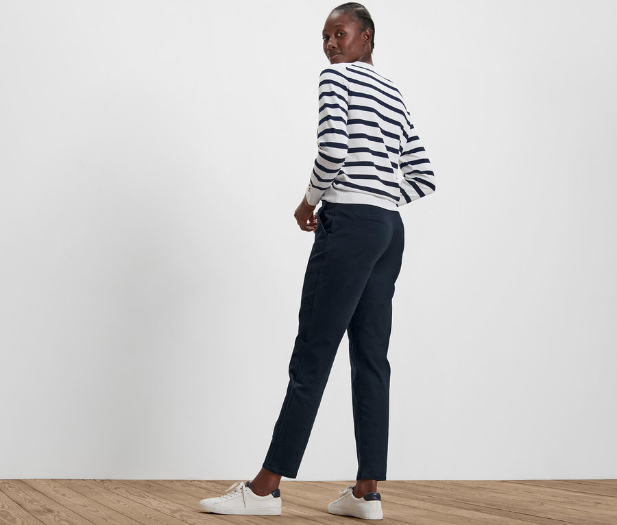 Frau blickt über die Schulter und trägt eine marineblaue Chino und ein gestreiftes Oberteil.