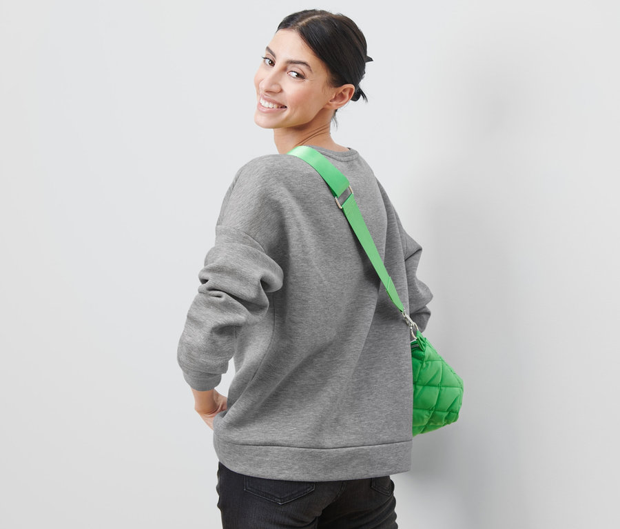 Frau blickt über die Schulter und trägt ein graues Sweatshirt mit Badge und eine grüne Tasche.