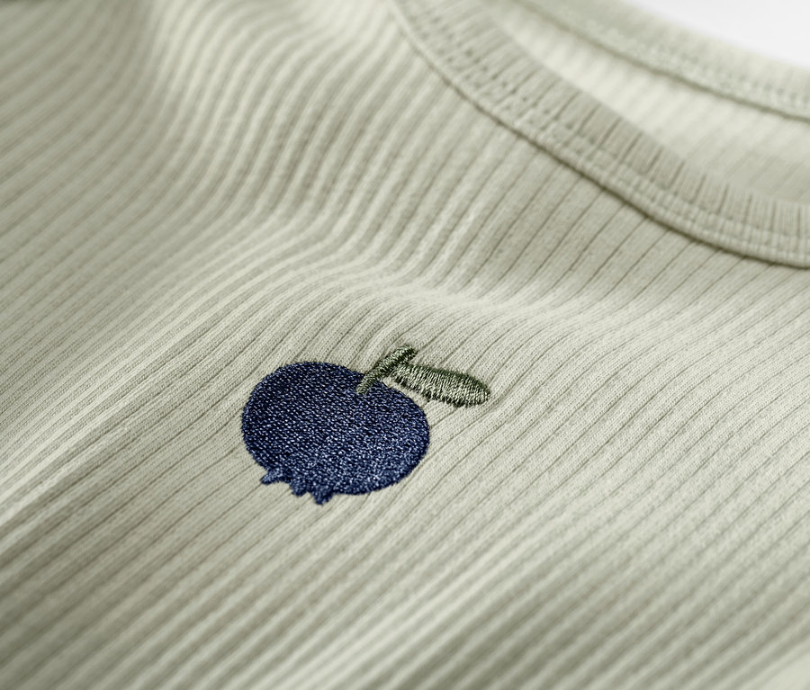 Detailaufnahme eines hellgrünen Baby-Langarmshirts mit einer blauen Apfelstickerei.