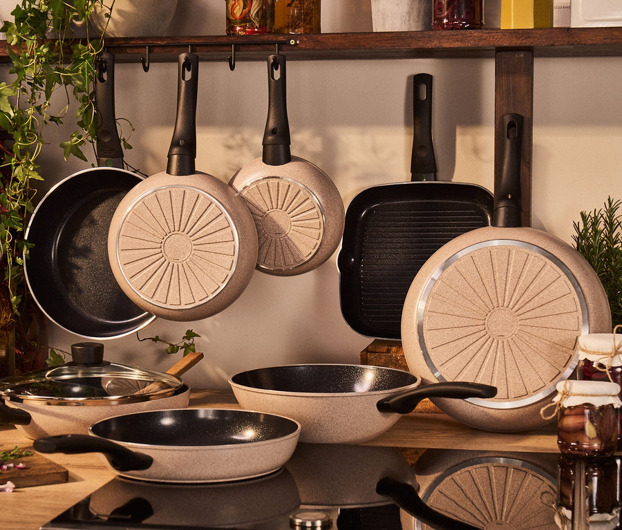 Verschiedene BALLARINI Pfannen hängen und stehen in einer Küche. BALLARINI Aluminium-Bratpfanne, sand, 20 cm.