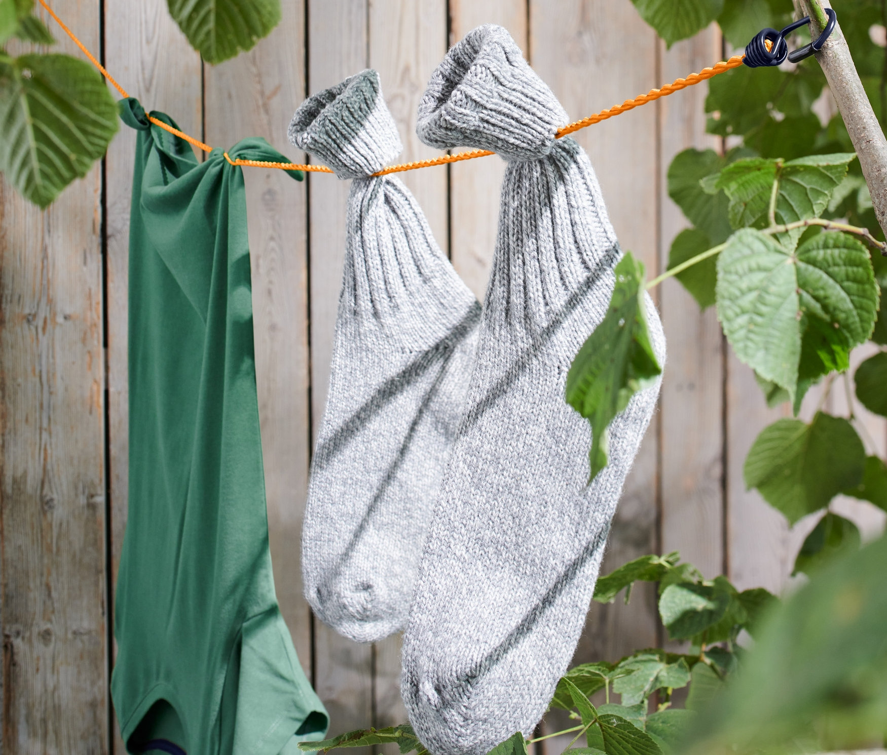 Ein grünes T-Shirt und ein Paar graue Socken hängen an einer Camping-Wäscheleine, die zwischen Ästen gespannt ist.