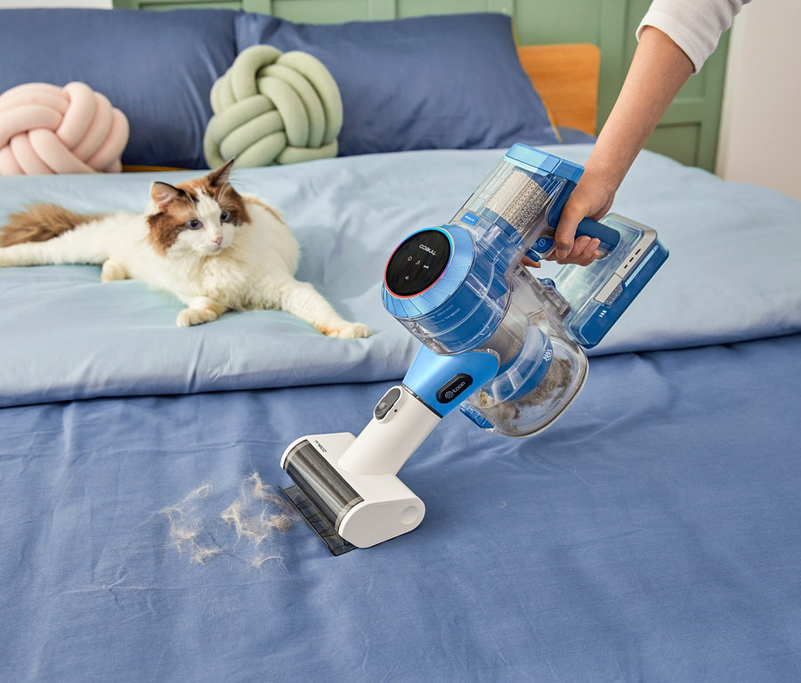 Eine Frau saugt mit einem Tineco Pure One S11 Akkusauger ein Bett ab, auf dem eine Katze liegt.