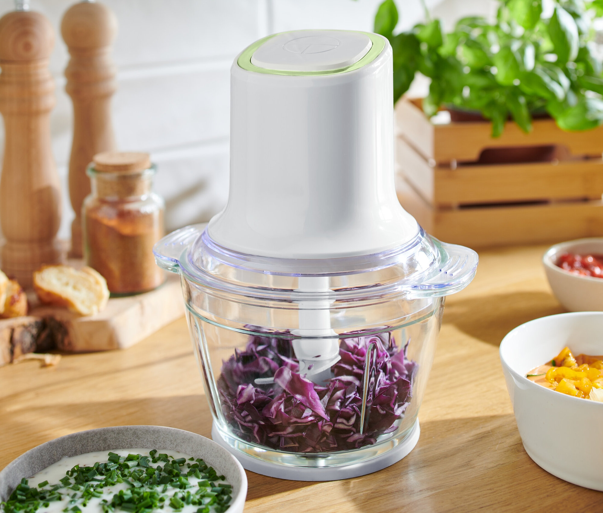 Ein Multizerkleinerer gefüllt mit geschnittenem Rotkohl steht auf einem Holztisch zwischen Schüsseln mit Soßen.