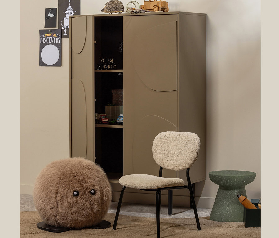 Ein Woood Lagerschrank »Cadiz« aus Kiefernholz steht in einem Kinderzimmer neben einem beige Stuhl und einem grünen Hocker.