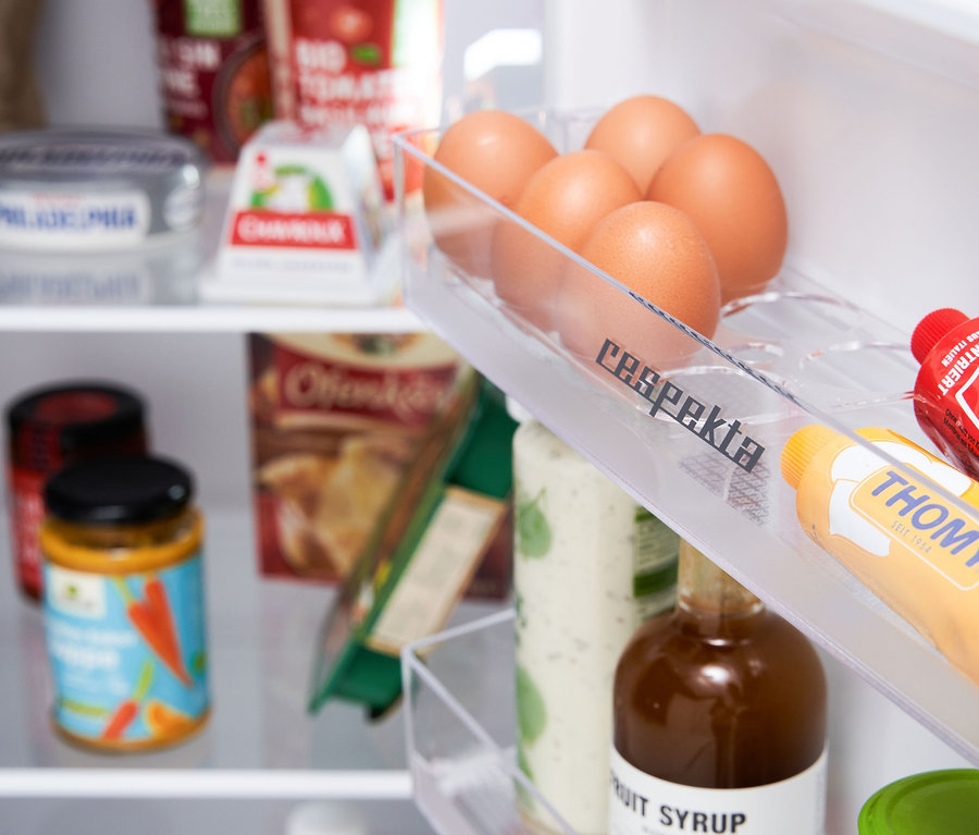 Ein Blick in einen Kühlschrank mit Eiern in einem durchsichtigen Halter, Mayonnaise und Ketchup in Tuben und verschiedenen Lebensmitteln im Hintergrund. Respekta Kühl-Gefrierkombination »KS144VC«, Vintage Cream ist sichtbar.