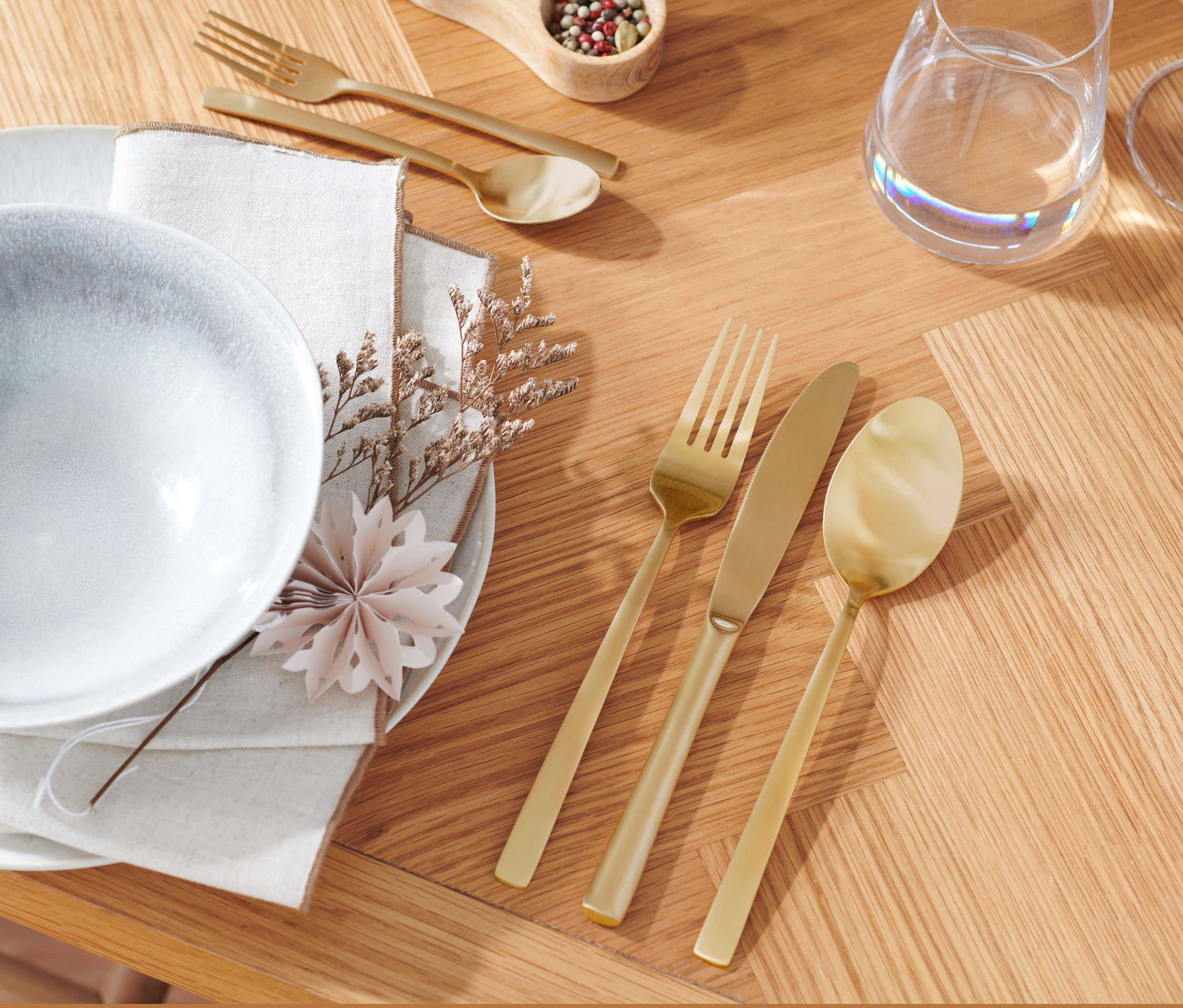 Teller, Serviette und 20-teiliges Besteck-Set in Champagnergoldfarbe auf einem Holztisch.