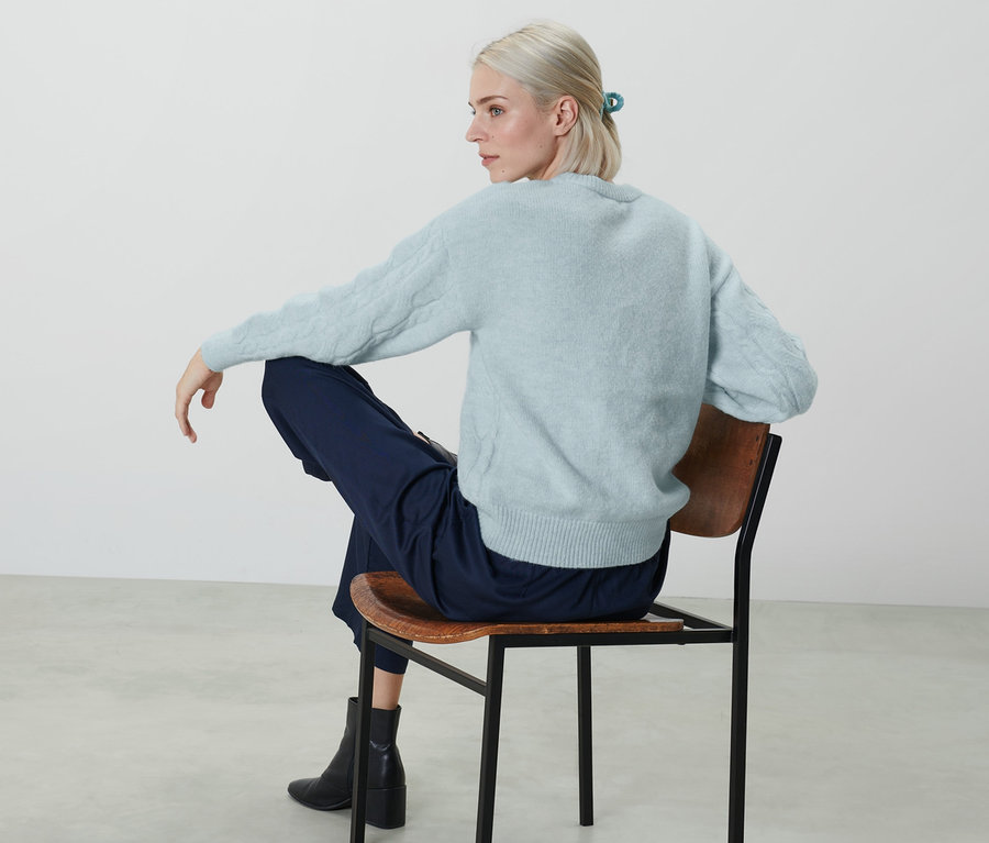 Frau sitzt auf einem Stuhl und trägt einen hellblauen Strickpullover.