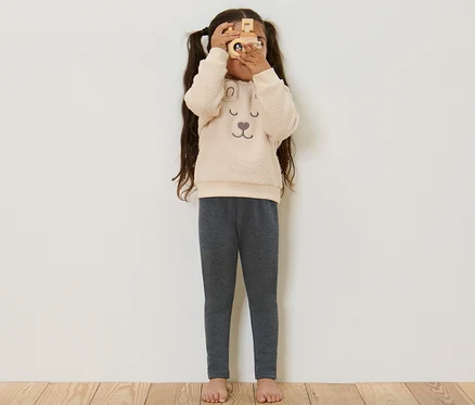 Mädchen schaut durch eine Holzkamera und trägt graue Kinder-Thermoleggings.