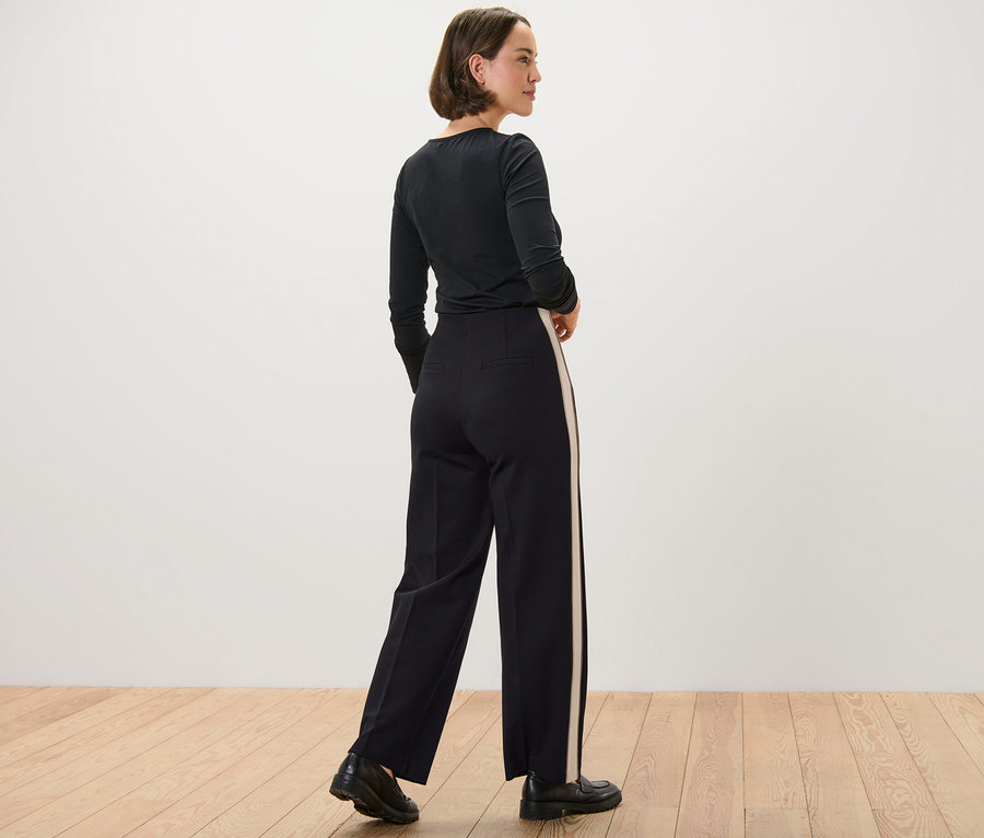 Frau in schwarzem Oberteil posiert in Jerseyhose mit Galonstreifen.