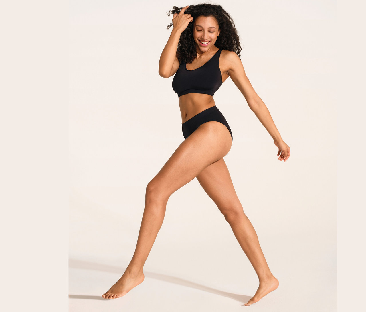 Frau geht und lächelt, sie trägt einen schwarzen SCHIESSER Soft BH mit Pads und einen schwarzen SCHIESSER Rio Slip.