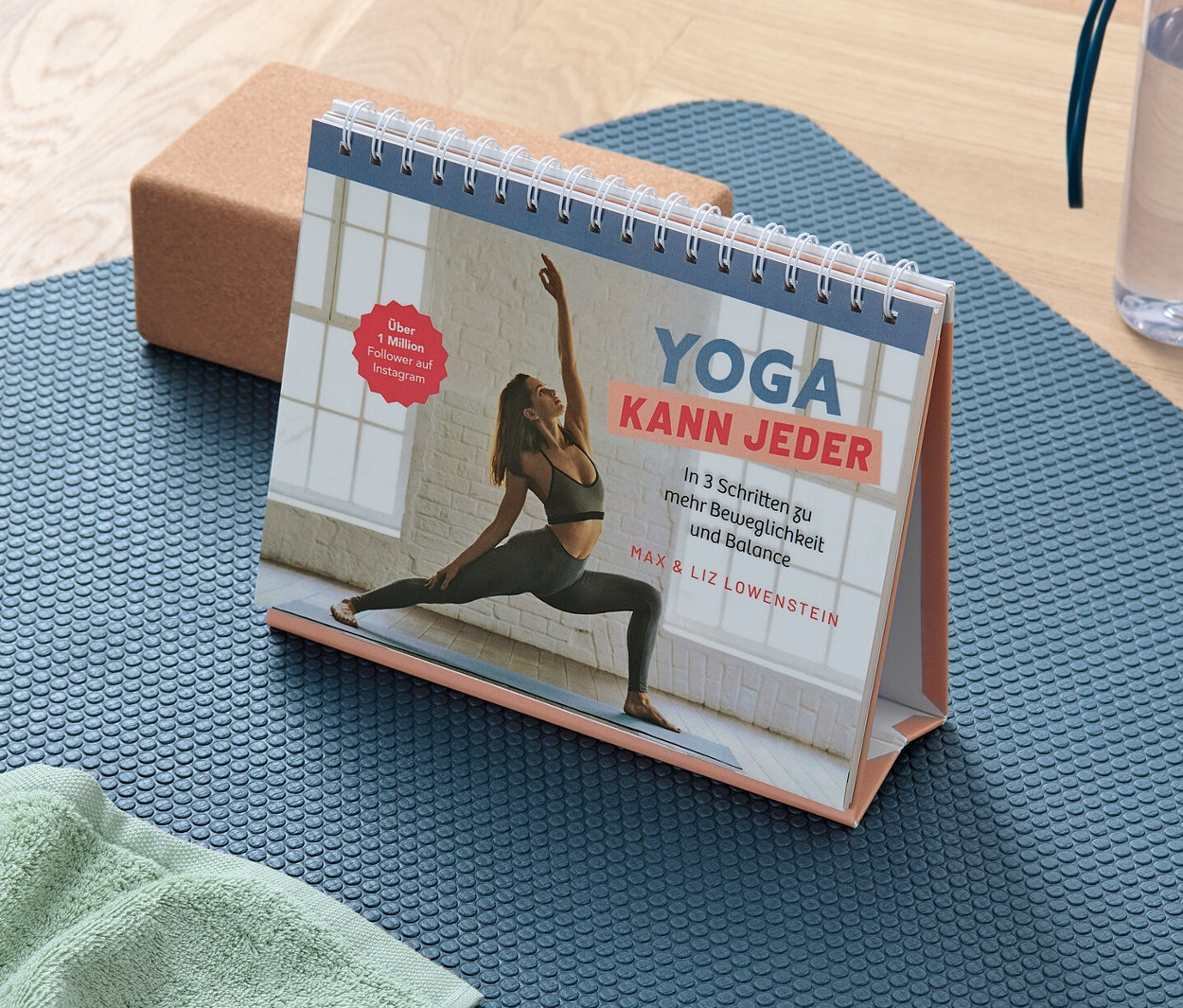 Eine blaue Yogamatte mit einem Handtuch, einem Block und dem Buch »Yoga kann jeder«.