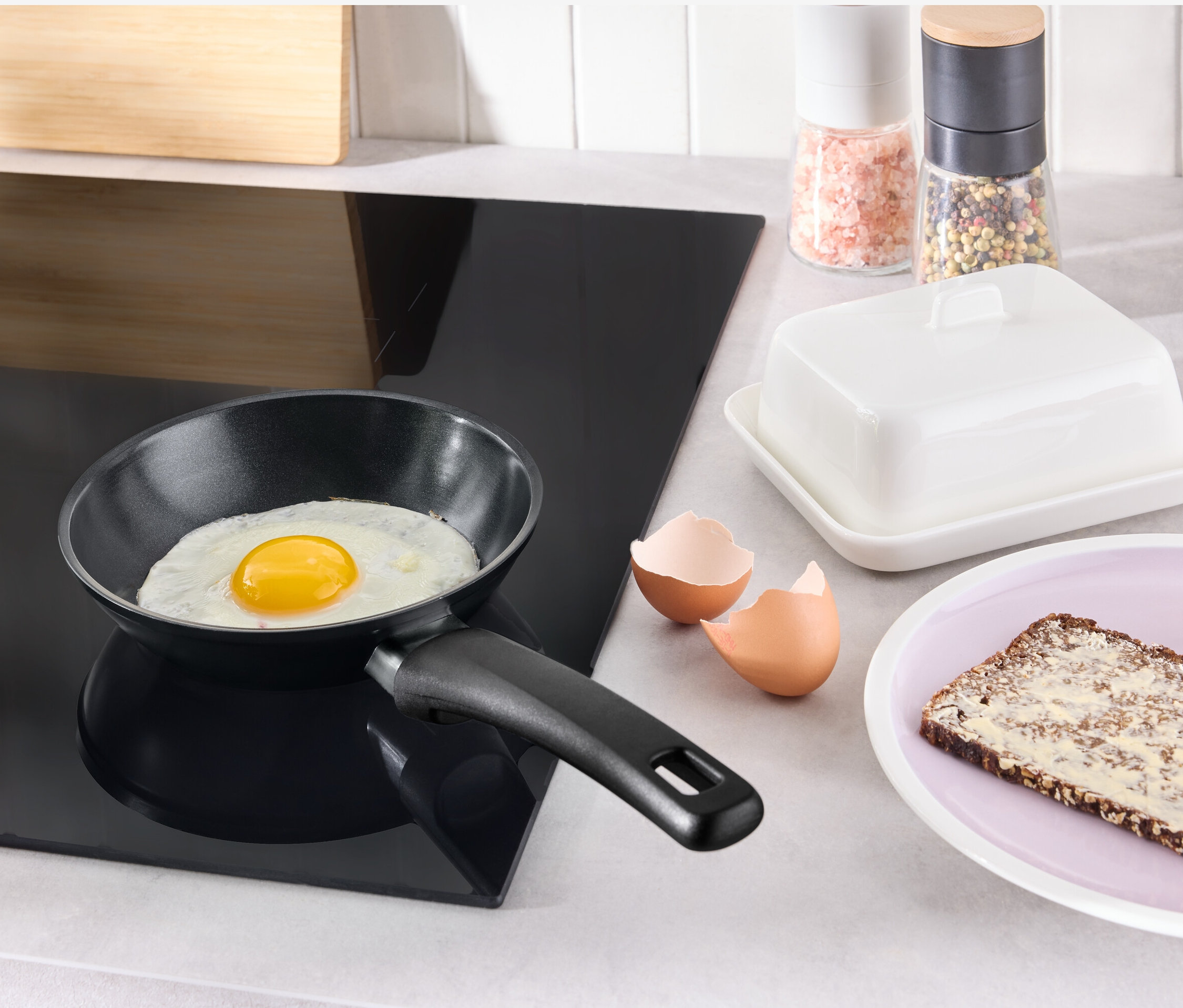 Auf einem schwarzen Kochfeld steht eine Mini-Pfanne mit Antihaftbeschichtung, in der ein Spiegelei brät.